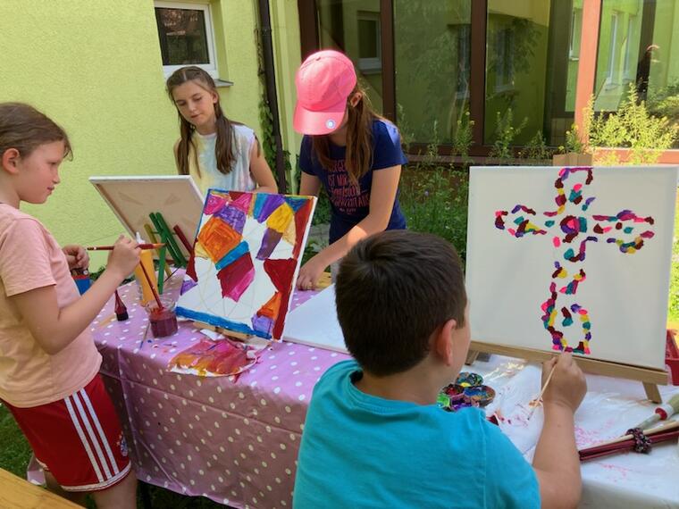 Vier Kinder malen im Freien auf Staffeleien bunte Acrylbilder.