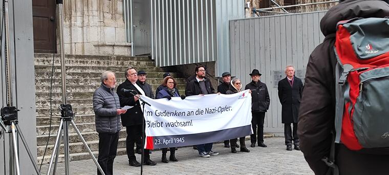 Eine Gedenkveranstaltung für die Opfer des NZ-Regimes: Menschen stehen mit Banner vor dem Westprotal des Regensburger Doms.