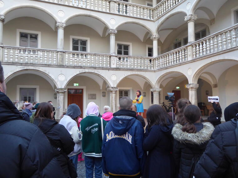 Eine Gruppen jungen Menschen hört einer Clownin zu, die im Innenhof des Thon Dittmer Palais in Regensburg ein Gedicht von Michael Ende vorträgt.